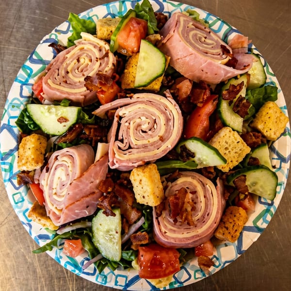 Overhead view of a hearty chef salad with rolled ham and cheese, bacon, croutons, lettuce, cucumbers, and tomatoes.