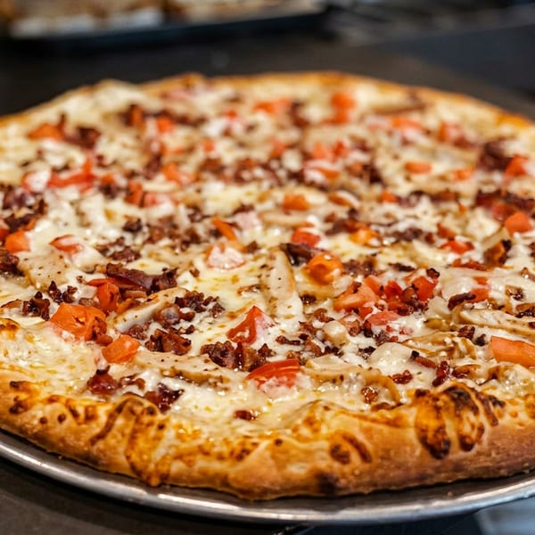 Large cheese pizza topped with diced tomatoes, chicken, and bacon on a metal serving tray.