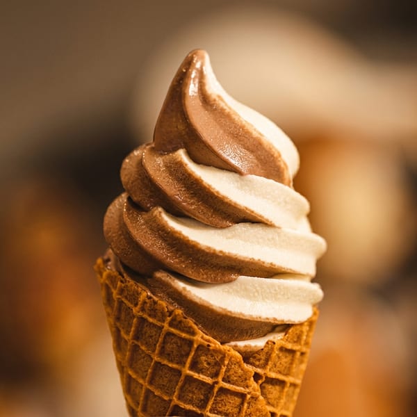 Swirled chocolate and vanilla soft-serve ice cream in a waffle cone against a warmly blurred background.