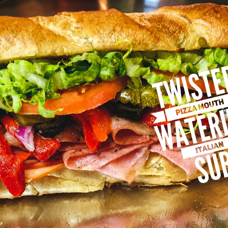Italian sub sandwich with lettuce, tomatoes, pickles, peppers, olives, and deli meats on a toasted baguette.