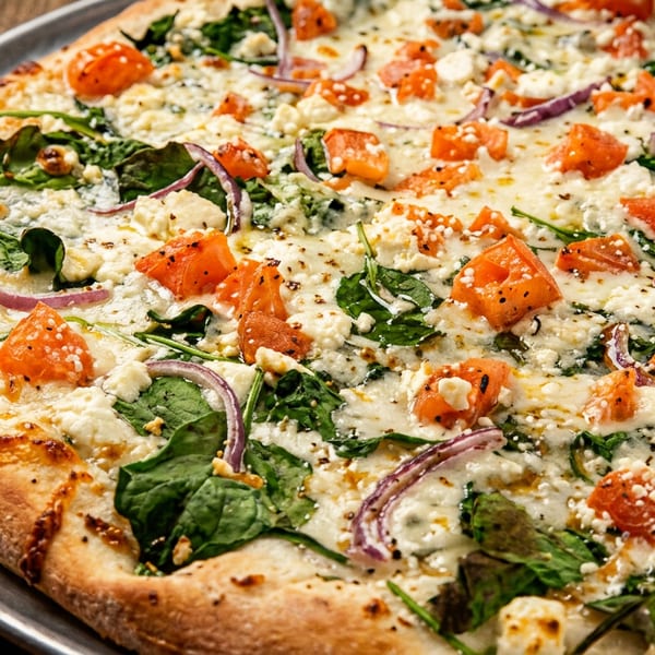 Close-up of a vegetable pizza topped with spinach, tomatoes, red onion, and crumbled white cheese on a metal tray.