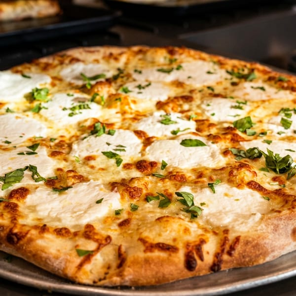Large golden-brown cheese pizza topped with creamy mozzarella and fresh herbs on a metal serving tray.