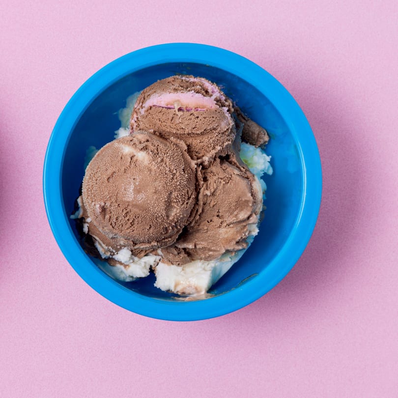 Scoops of chocolate and vanilla ice cream in a bright blue bowl on a pink background.