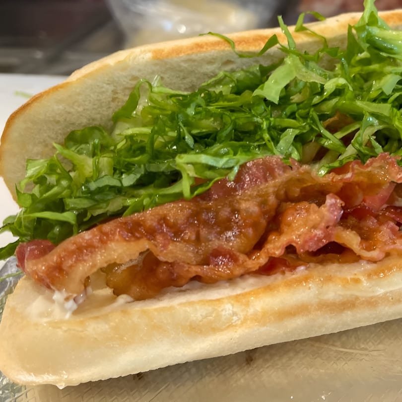 Close-up of a Twisted Pizza sub with crispy bacon, fresh lettuce, and creamy sauce on a toasted bun.