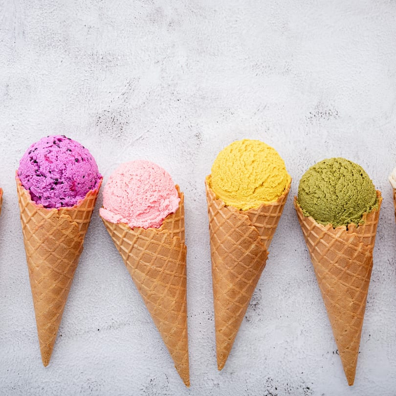 Four colorful scoops of Twisted Pizza ice cream in waffle cones on a white background.