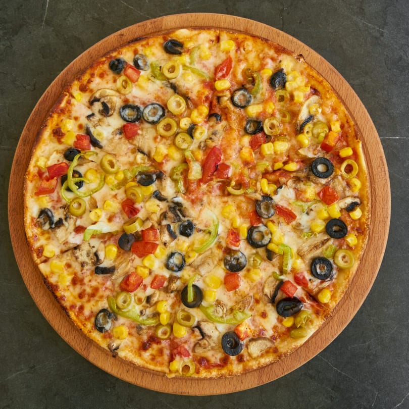 Twisted Pizza's vibrant veggie pizza, topped with olives, corn, peppers, and mushrooms on a wooden board.