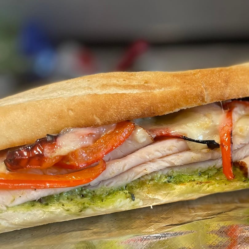 Close-up of a Twisted Pizza sub with melted cheese, red peppers, and green pesto.