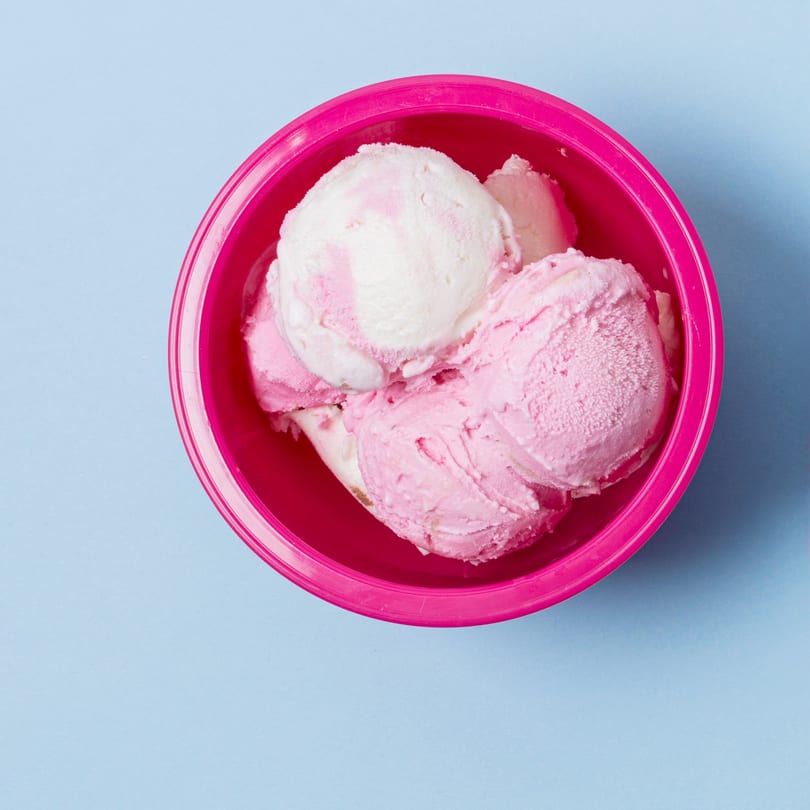 Scoops of pink and white ice cream in a bright pink bowl on a light blue background.